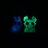 Two small, glowing resin figures from Bindlewood Shop are seen in the dark: Sunshower Moose with antler-like features and Plasma Storm Chenille with bunny-like ears, both from the Sunshower Moose & Plasma Storm Chenille Set.