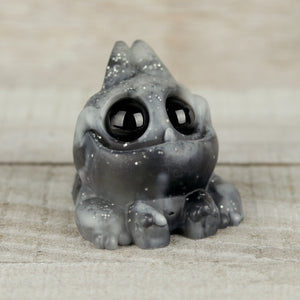 The Thundersparkle Tank by Chris Ryniak is a small, round gray resin figure with large black eyes, white speckles, and a glossy finish, shown resting on a light wooden surface.