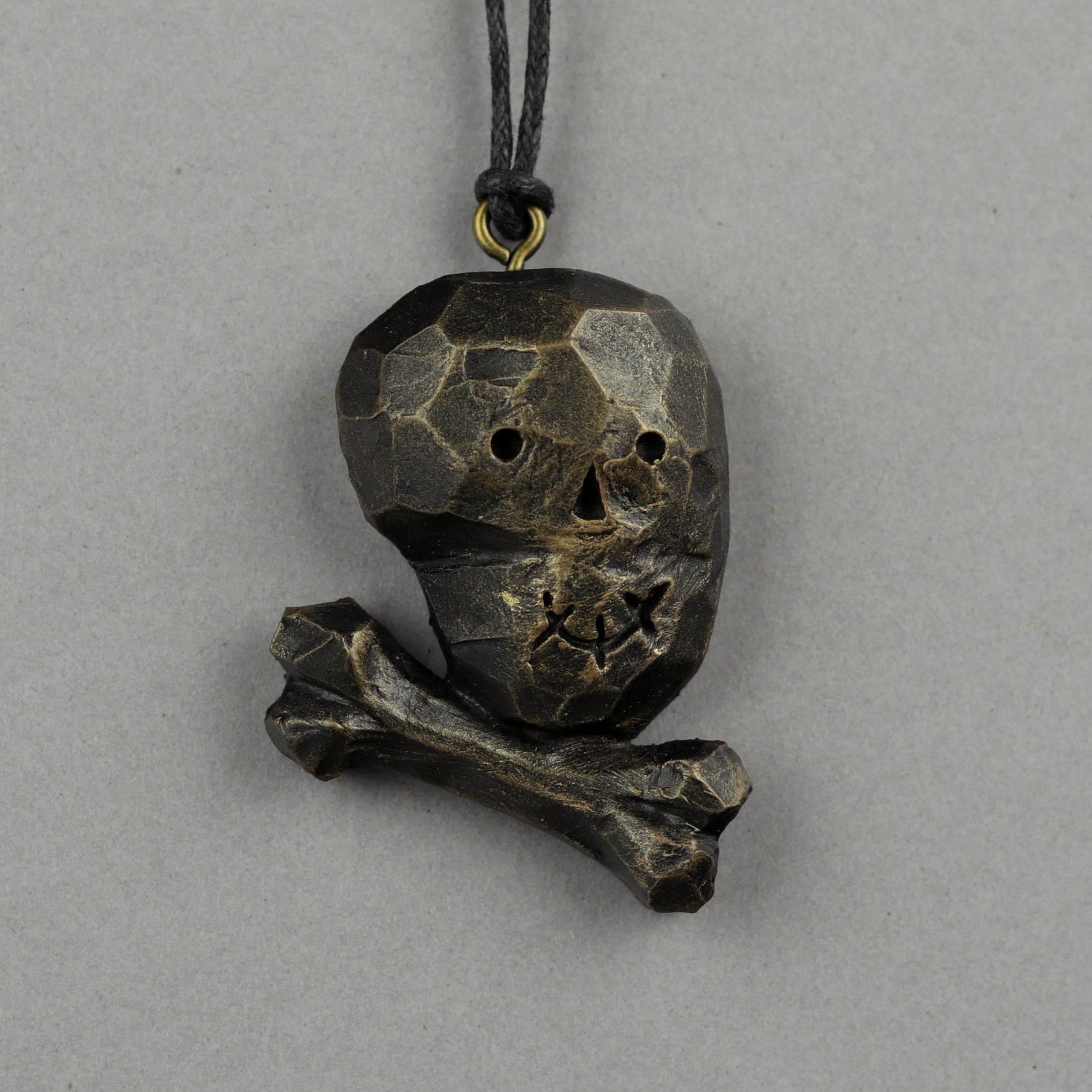 The Bindlewood Shop Painted Mini Ornaments feature a faceted, angular skull and crossbones pendant made of dark, textured metal, hanging from a black cord against a plain grey background.