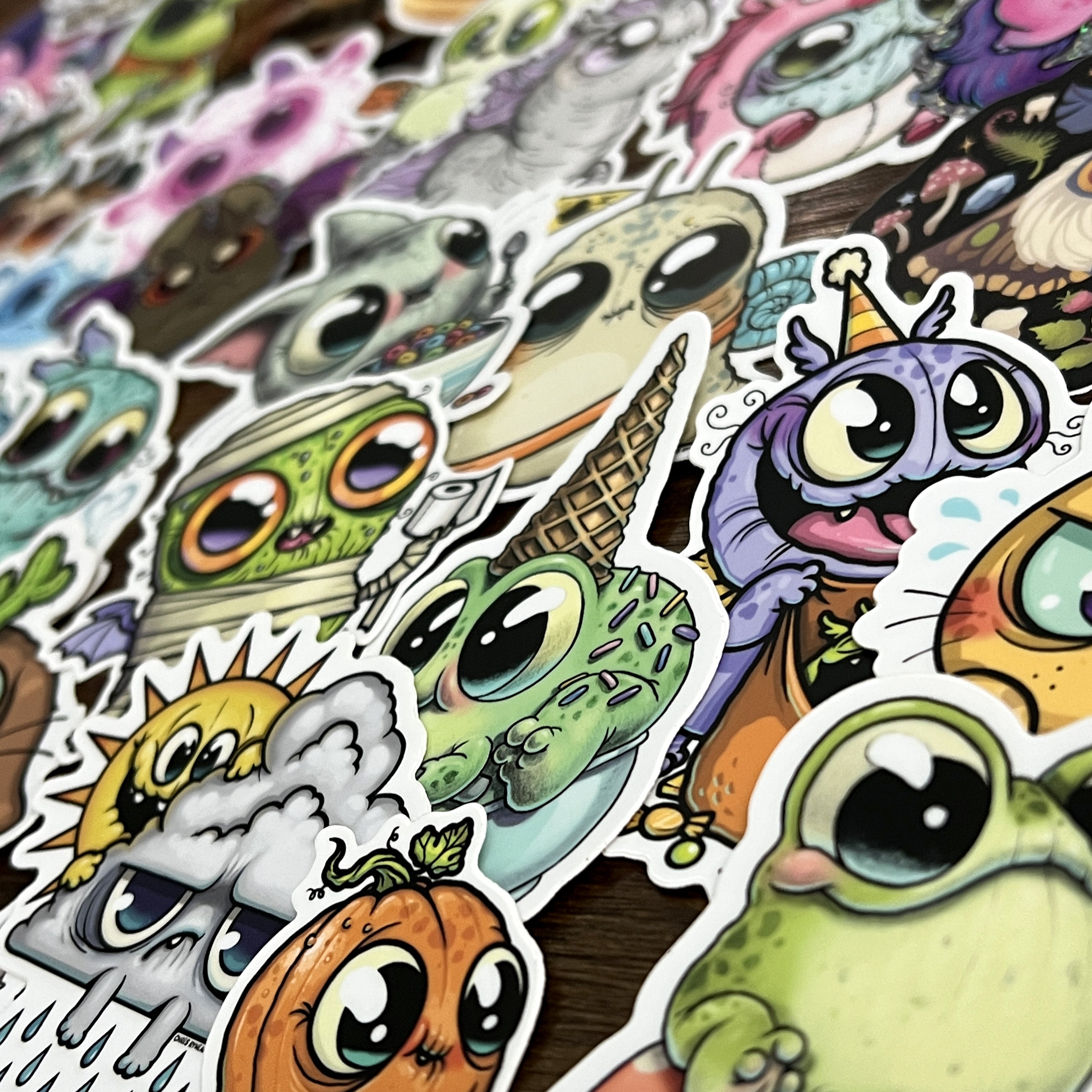 The ULTRA MEGA STICKER PACK! by Bindlewood Shop showcases a lively assortment of cute, big-eyed cartoon creatures—such as frogs, pumpkins, and quirky animals—all clustered together on a flat surface. These playful vinyl stickers are ideal for adding personality to your laptop, notebook, or water bottle.