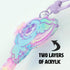 Close-up of the colorful, cartoon-style Flooficorn Keychain from Bindlewood Shop, shaped like an animal with big eyes and made from two thick layers of reflective acrylic. A black arrow and text say “TWO LAYERS OF ACRYLIC.”.
