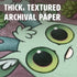 Close-up of Amanda L Spayd's Aries Zodiac Print, showing a vibrant creature with big green eyes on thick, textured archival paper. "Thick, Textured Archival Paper" is displayed at the top of the image.