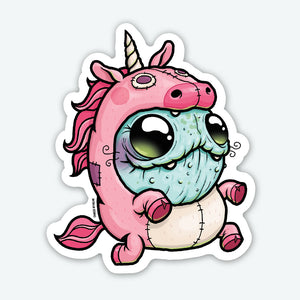 The Unicorn Suit Sticker from Bindlewood Shop features a stuffed, blue-skinned cartoon character with large eyes and a droopy mouth, dressed in a whimsical pink unicorn onesie complete with a horn, ears, mane, and tail. This sticker captures an adorable yet odd appearance that would make for high-quality stick-on decorations.