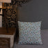 A Bindlewood Shop Twilight Sprite Throw Pillow with a floral pattern rests on a neatly made bed with a gray quilt. The headboard of the bed is upholstered with gray fabric. A wooden nightstand with a lamp, featuring nature-themed wallpaper in the background, complements the cottagecore interior design.