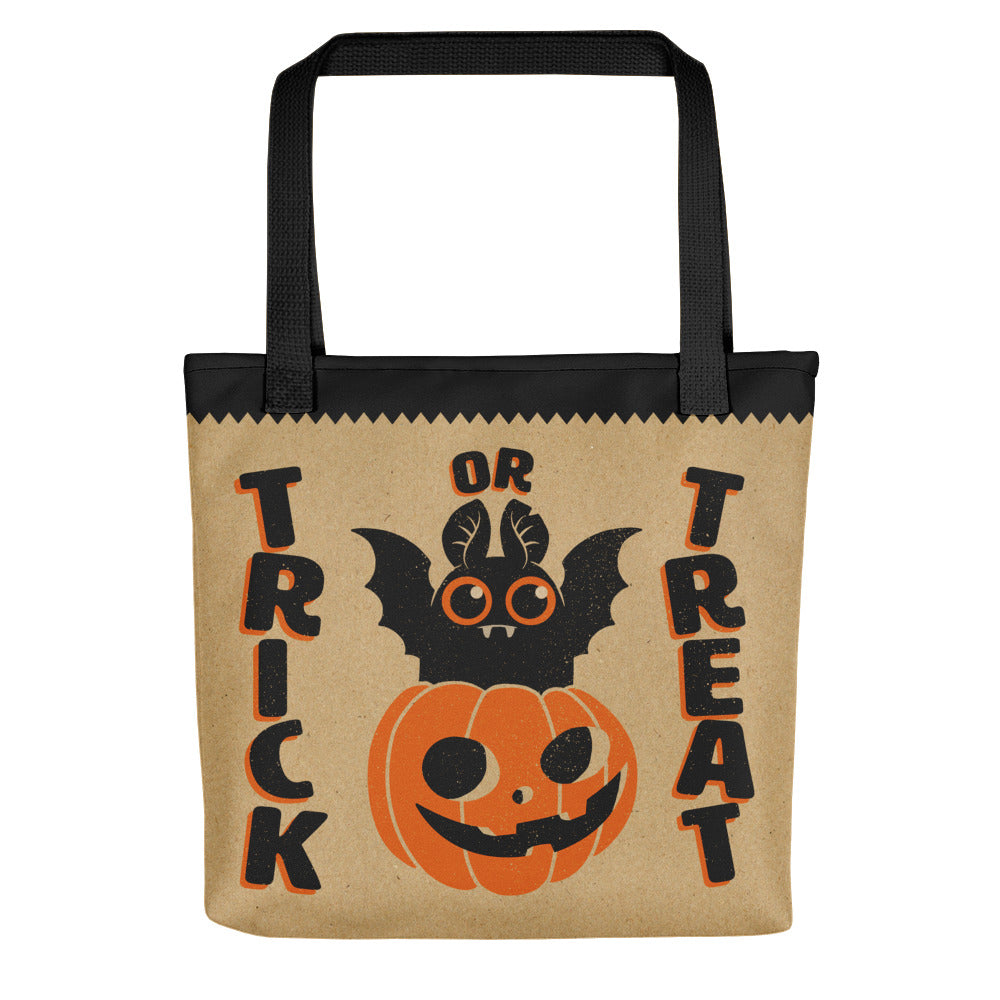 The Bindlewood Shop Halloween Tote is a tan candy bag with black handles, featuring a smiling jack-o’-lantern, cartoon bat, and bold “Trick or Treat” text—perfect for carrying treats on Halloween.