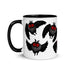 A white ceramic mug with a black handle and rim, this Mothman Cryptid Mug from Bindlewood Shop features a repeating pattern of a cartoonish black owl with bright red eyes, flapping wings, and feather tufts on its head. The owl image is displayed multiple times in a scattered arrangement, perfect for any cryptozoology researcher.