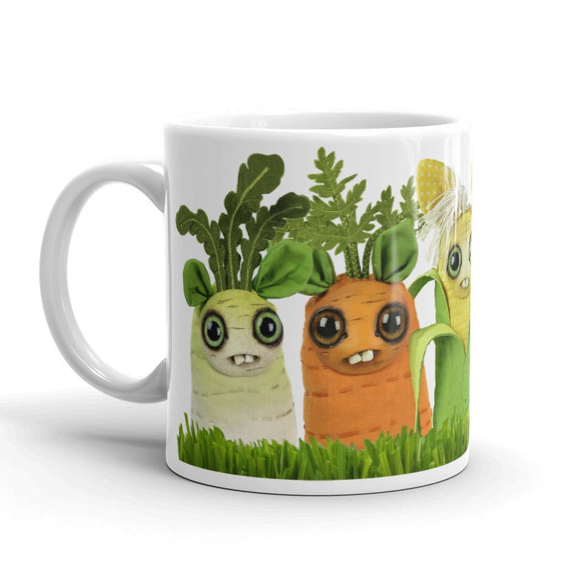 The Farm Market Dust Bunnies Mug by Bindlewood Shop is a charming white ceramic mug featuring adorable cartoon vegetables with faces and big eyes, including a green leafy veggie, a smiling carrot, a yellow corn cob with hair-like husks, and another leafy plant standing in grass. Dishwasher-safe and microwave-safe, it's perfect for everyday use.