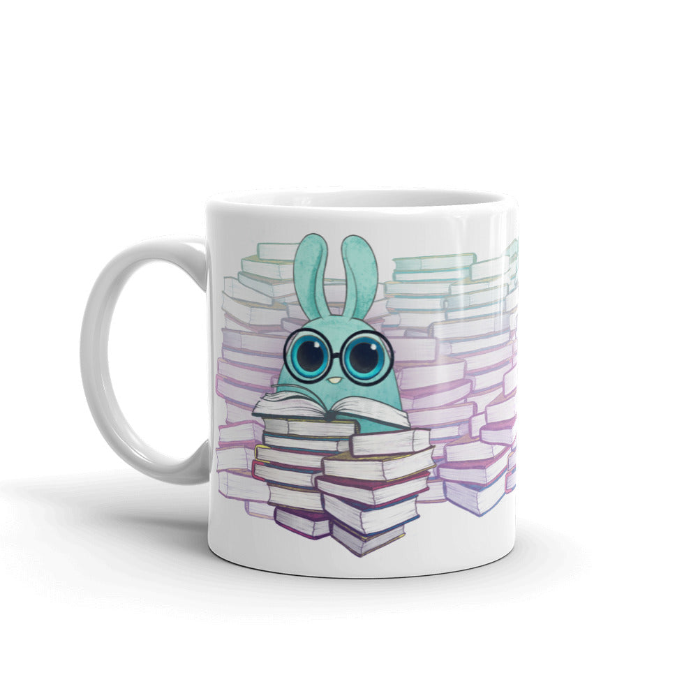 The So Many Books Mug from Bindlewood Shop features an adorable blue cartoon bunny with big eyes and glasses, engrossed in reading a book. The charming design, surrounded by towers of books, creates a delightful and whimsical reading atmosphere. Additionally, it's both dishwasher and microwave safe for extra convenience.